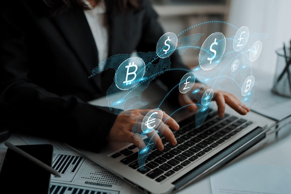 Business professional using laptop with virtual currency icons Including Bitcoin, Euro, Dollar, and Pound.