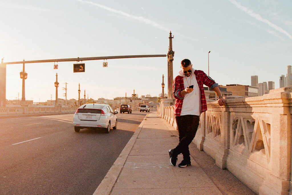 A man leans against a decorative railing on a bridge as a car passes by.