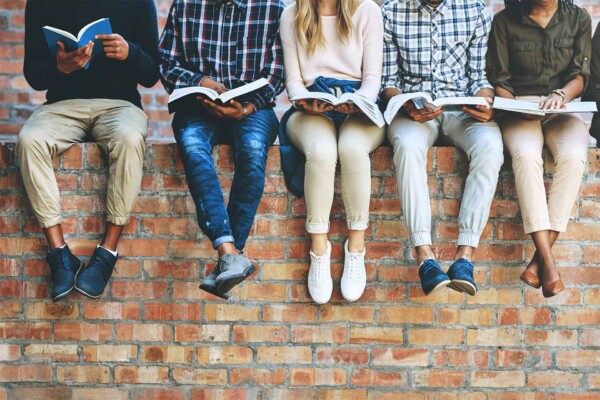 Several students sitting on a brick wall, reading books.