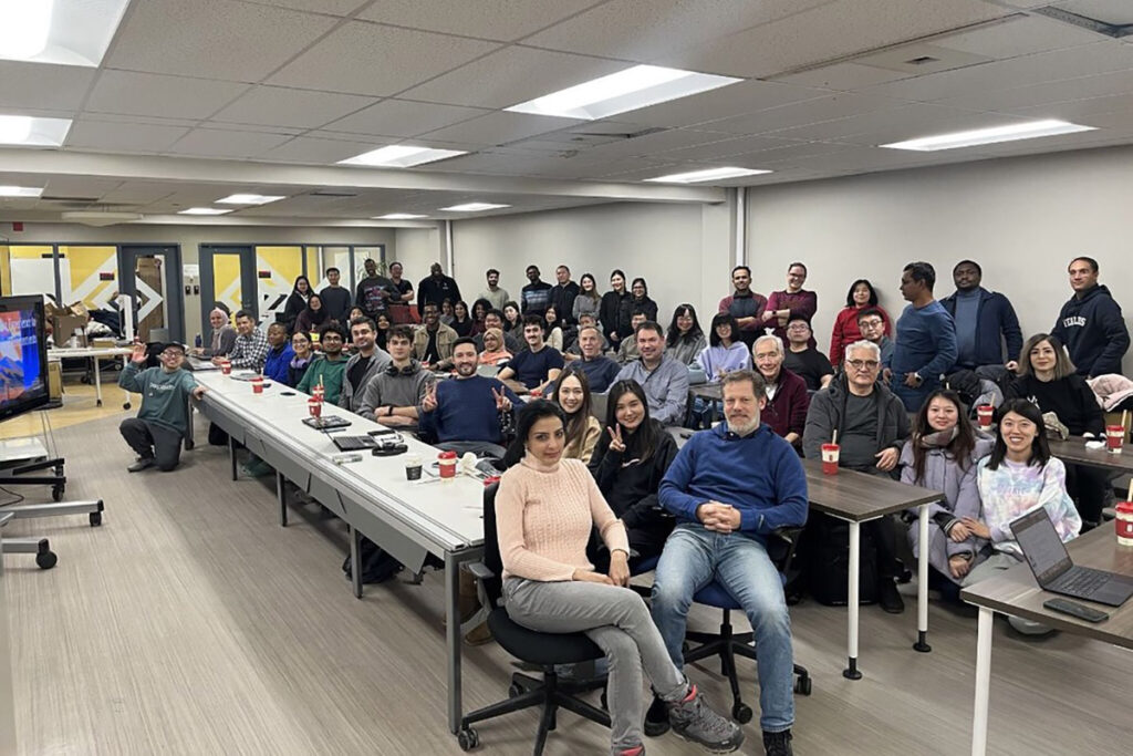 A very large group of people pose for a picture while seated in a classroom.