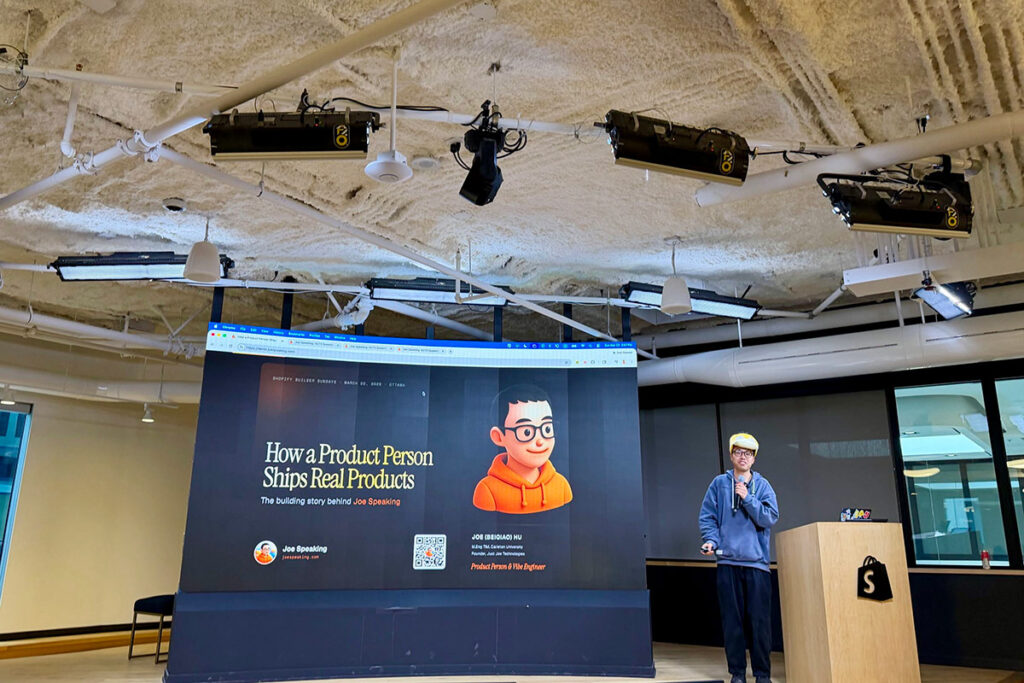 A man delivers a speech next to a podium, with a large screen next to him.