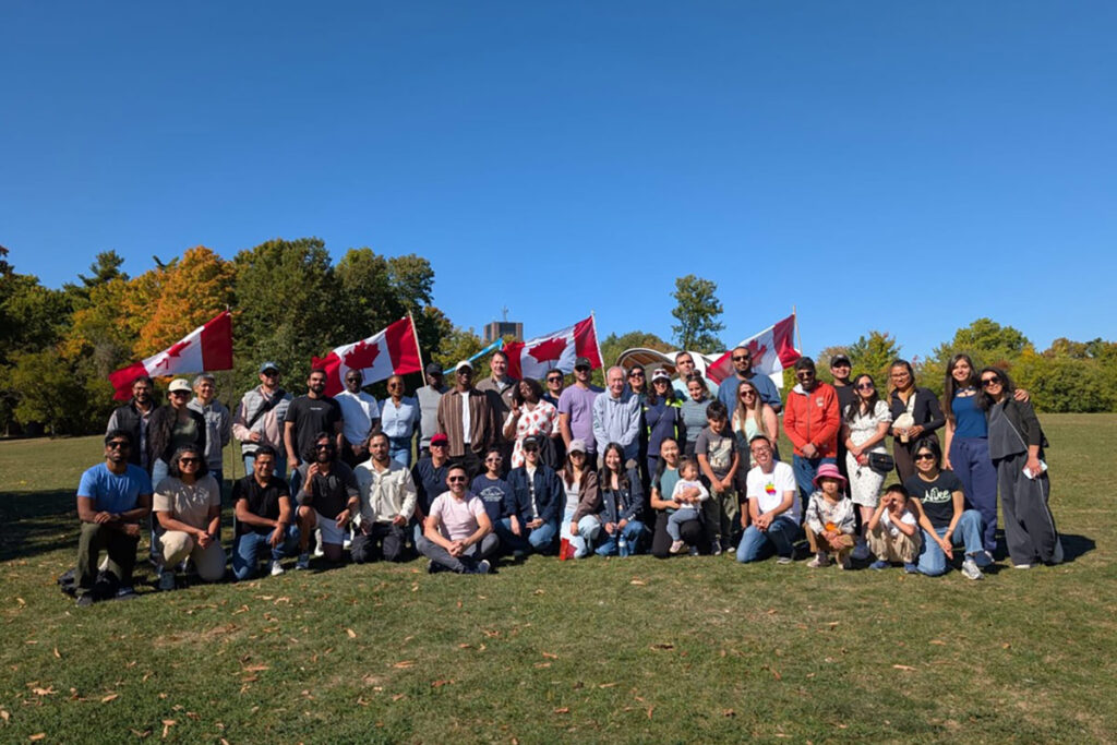 A large group of people pose for a photo with four Canadian flags visible behind them.