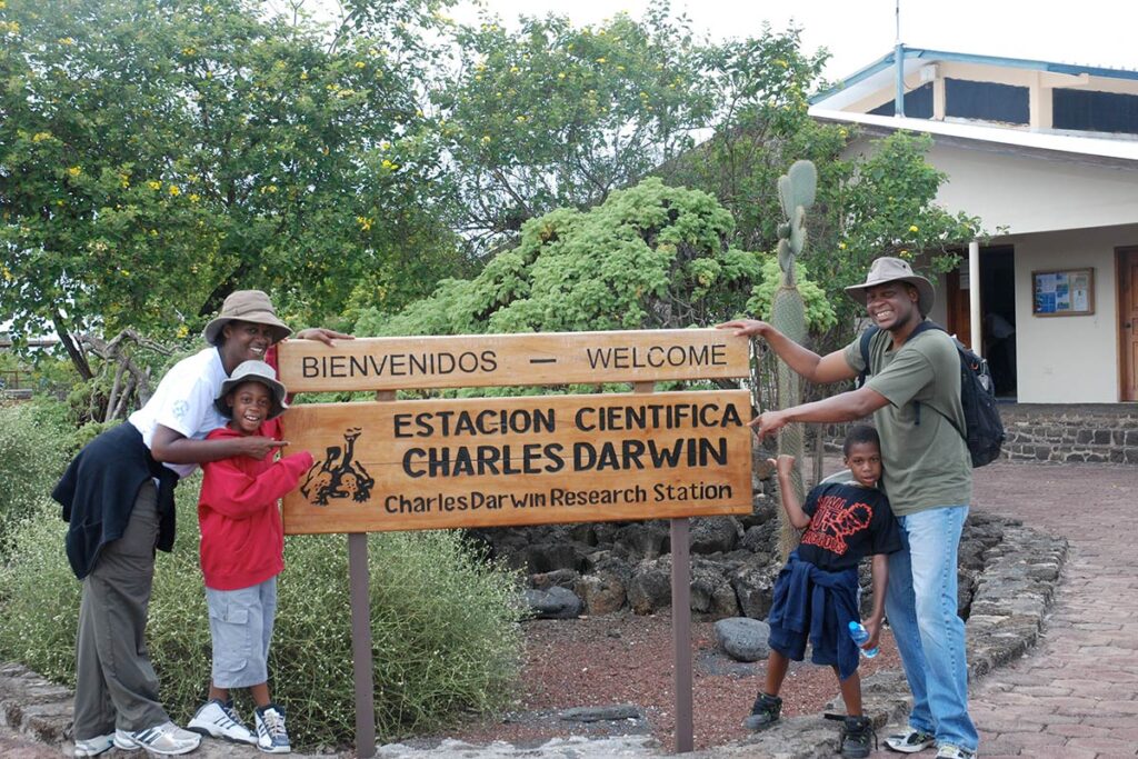 Four people posing with a sign that reads Charles Darwin Research Station.