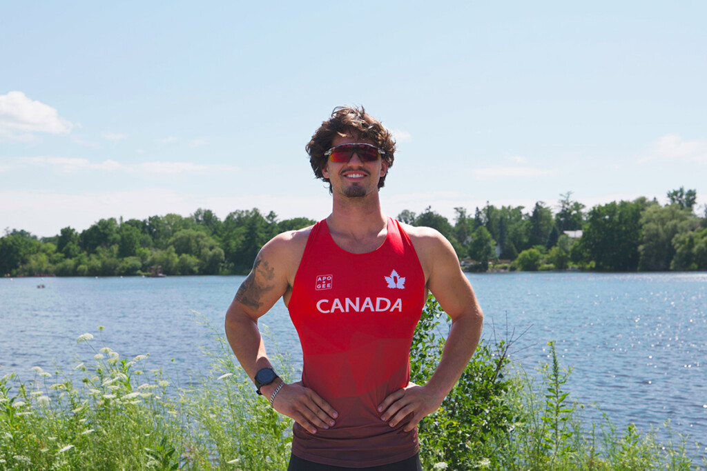 An athlete in a red uniform poses for the camera in front of a lake.