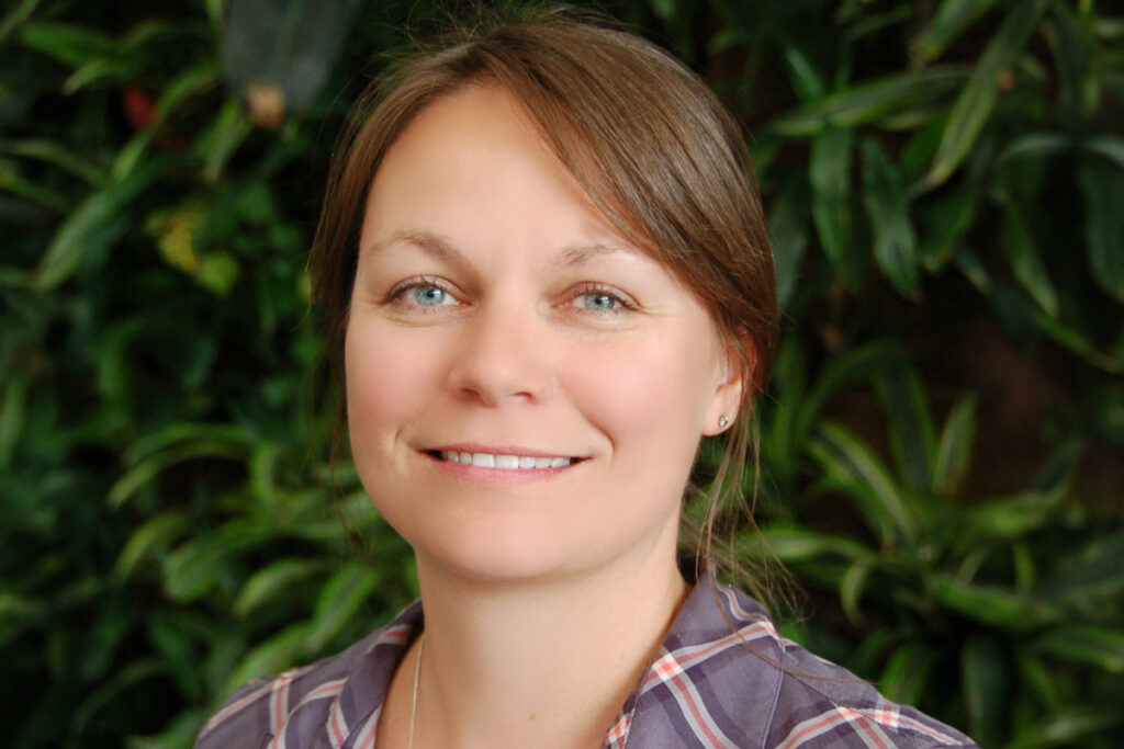 A headshot of a woman standing in front of a large group of plants.