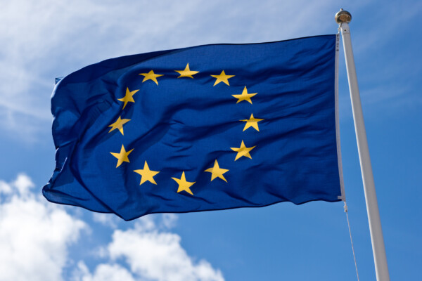 The European Union flag on a post, flying against a backdrop of a cloudy sky on a windy day.