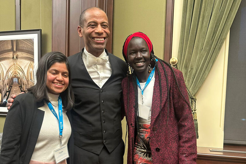 Nyabuol Biel Gang, wearing a red headband and coat, stands with two other people.