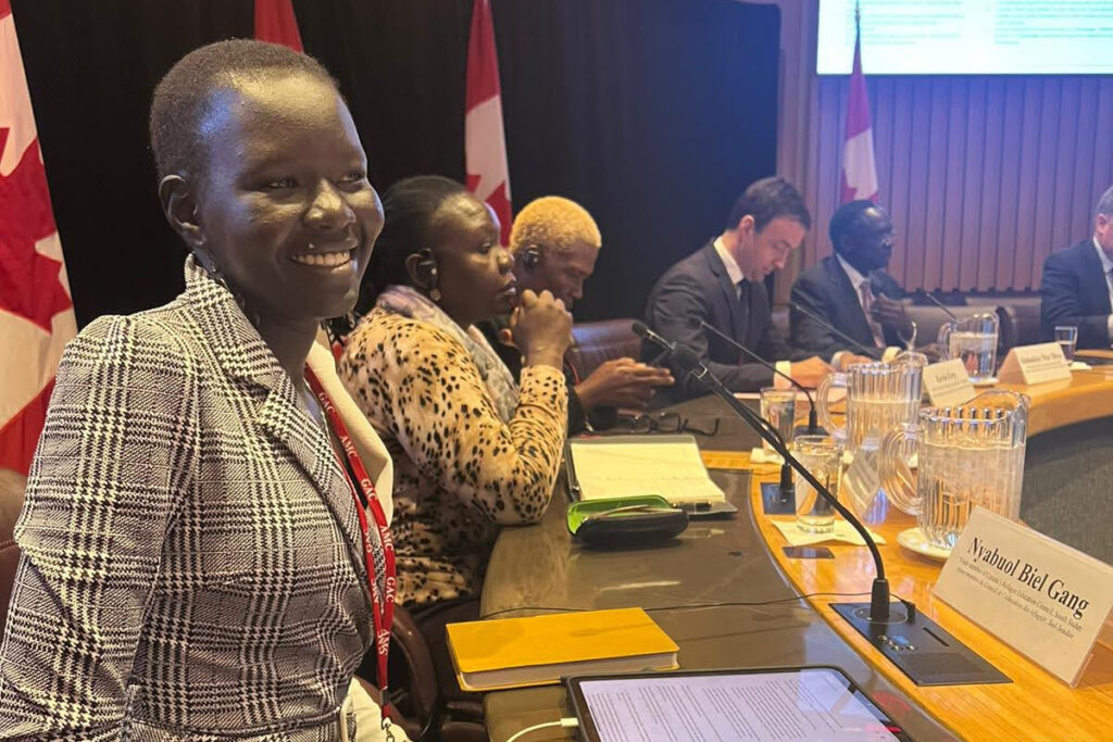 Nyabuol Biel Gang smiles at a meeting table beside a name card bearing her name.