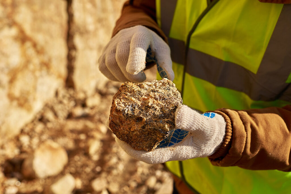 Close up of industrial worker holding mineral ore in gloved hands on mining site.