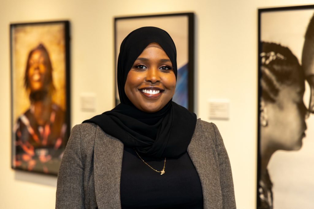 Faisa Omer poses for a photo in front of framed photos from her "Threading Roots" exhibition.