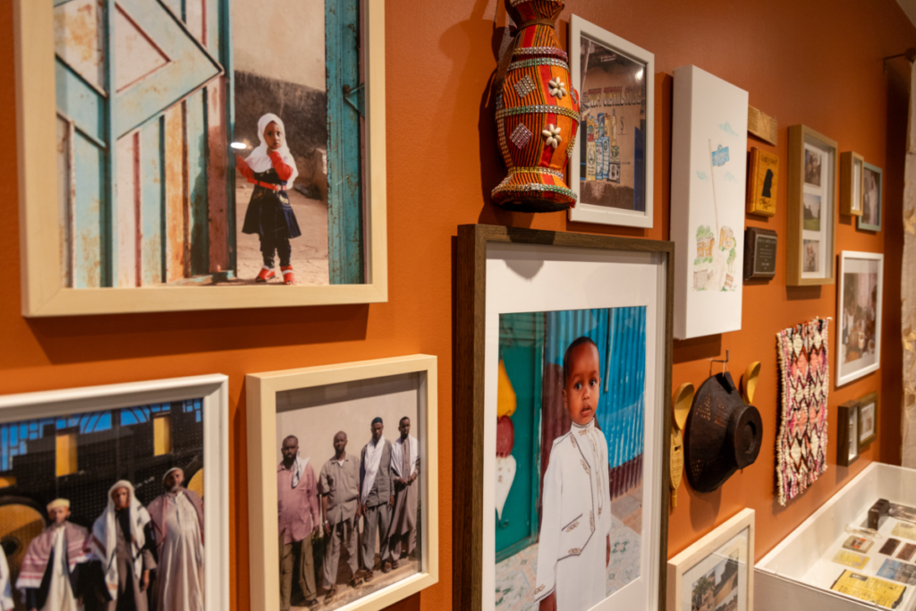 Portraits and art pieces hanging on an orange wall as part of Omer's "Threading Roots" exhibit. 
