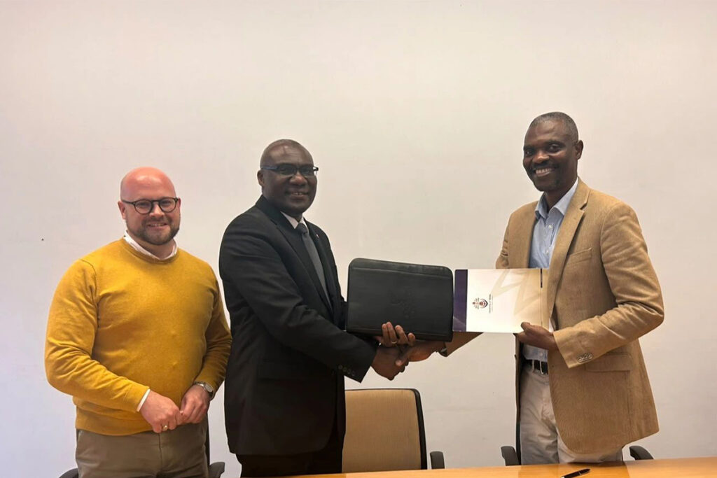University representatives shake hands while displaying a signed collaboration agreement.