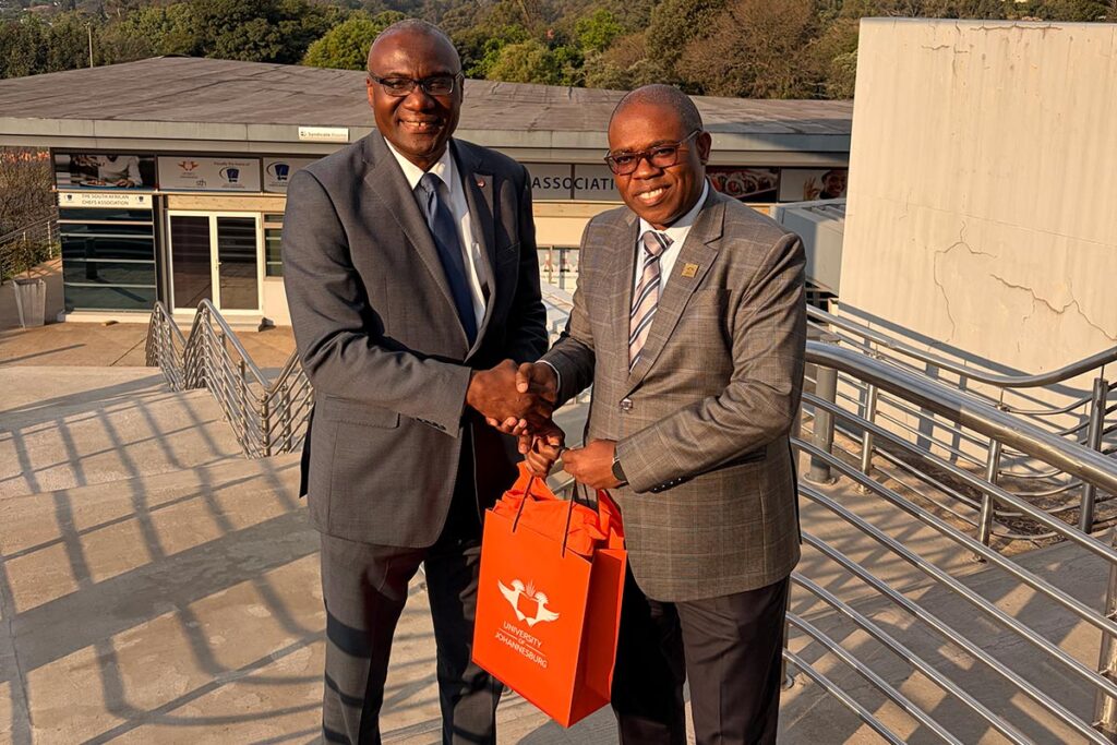 Wisdom Tettey exchanges a gift with a South African university representative outdoors.