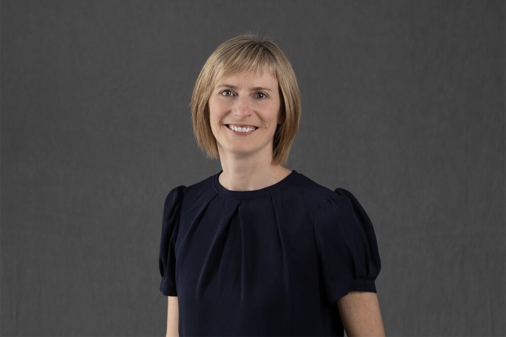 Woman with short blonde hair smiling against a grey backdrop.