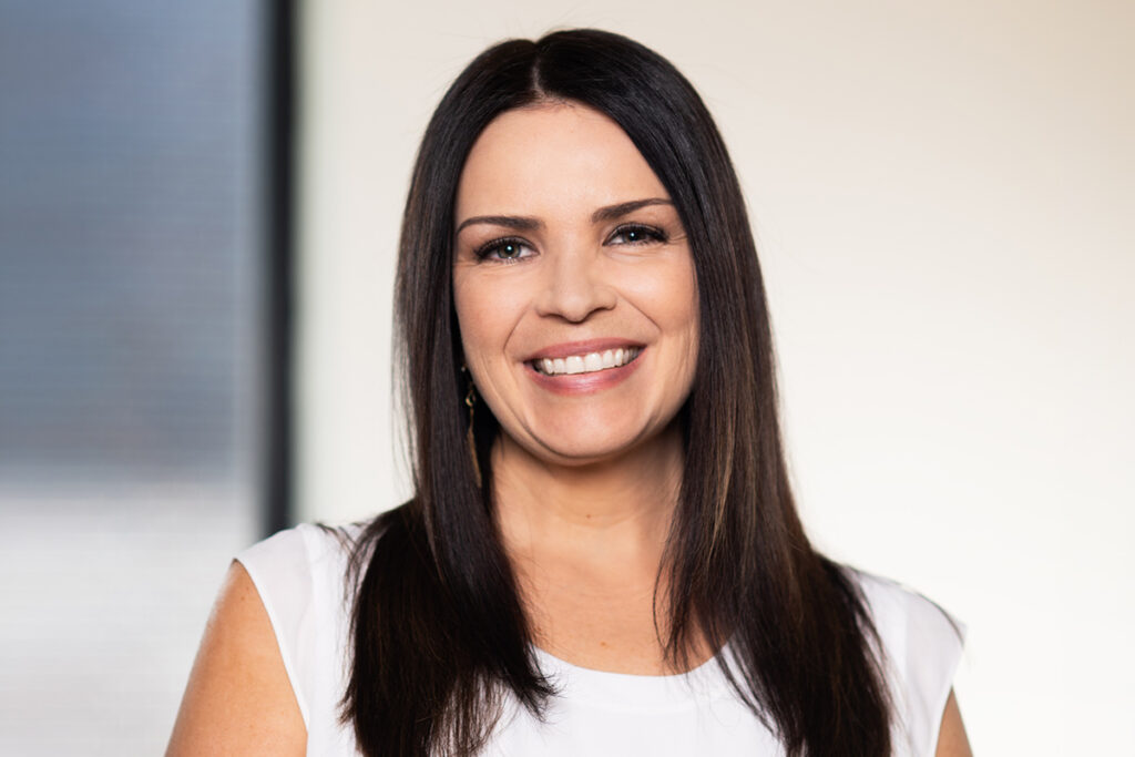 Woman with long dark hair smiling in a white top.