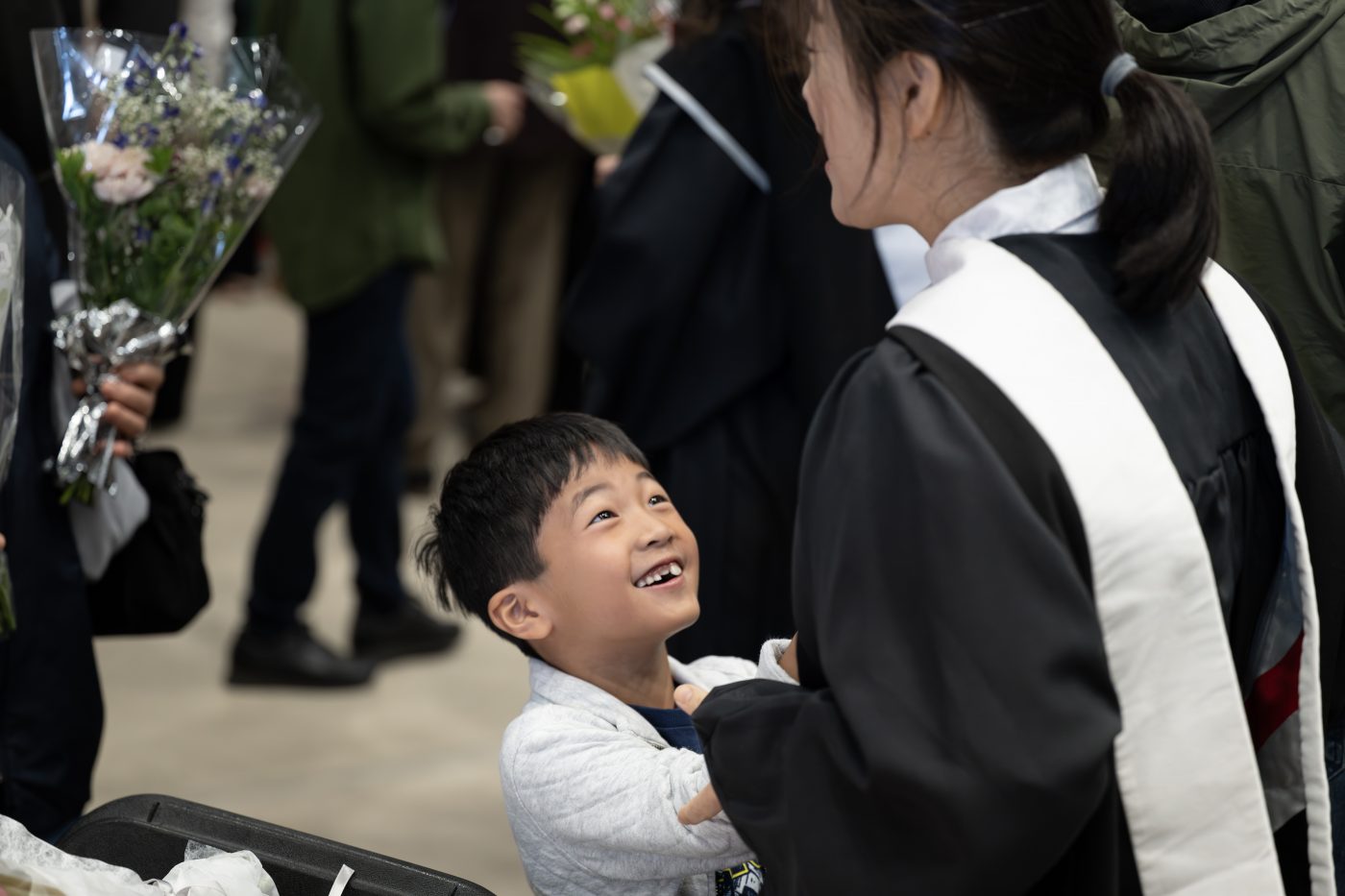 A child smiles at a woman in a graduation gown.