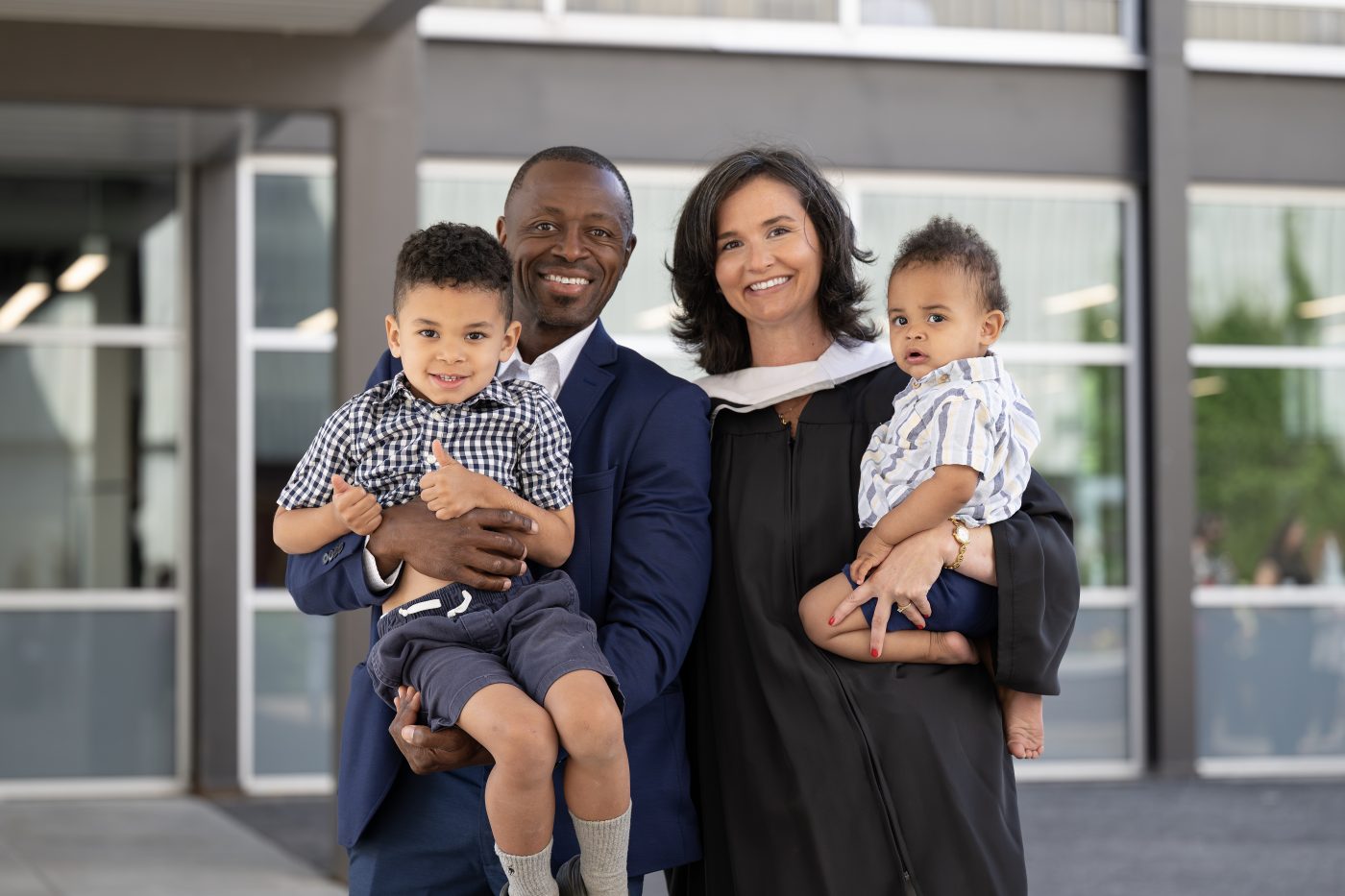 A recent graduate poses with her partner and two children outside the Athletics building.