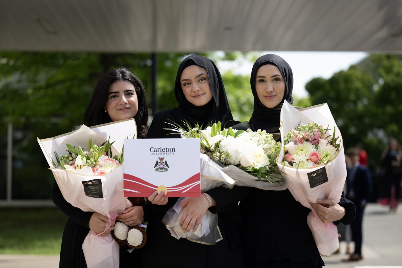 Graduating students pose with their bouquets and cu_people_degree outside the Athletics building.