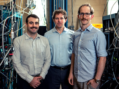 The FlareNet teams poses in their lab surrounded by electronic gear and monitoring equipment.