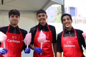 Three men wear red aprons and hold cotton candy