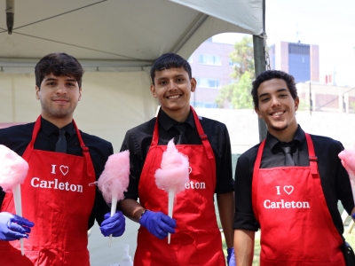 Three men wear red aprons and hold cotton candy