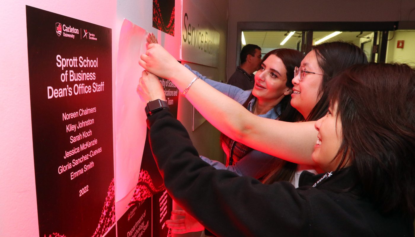 Three women placing an sticker award on a wall board