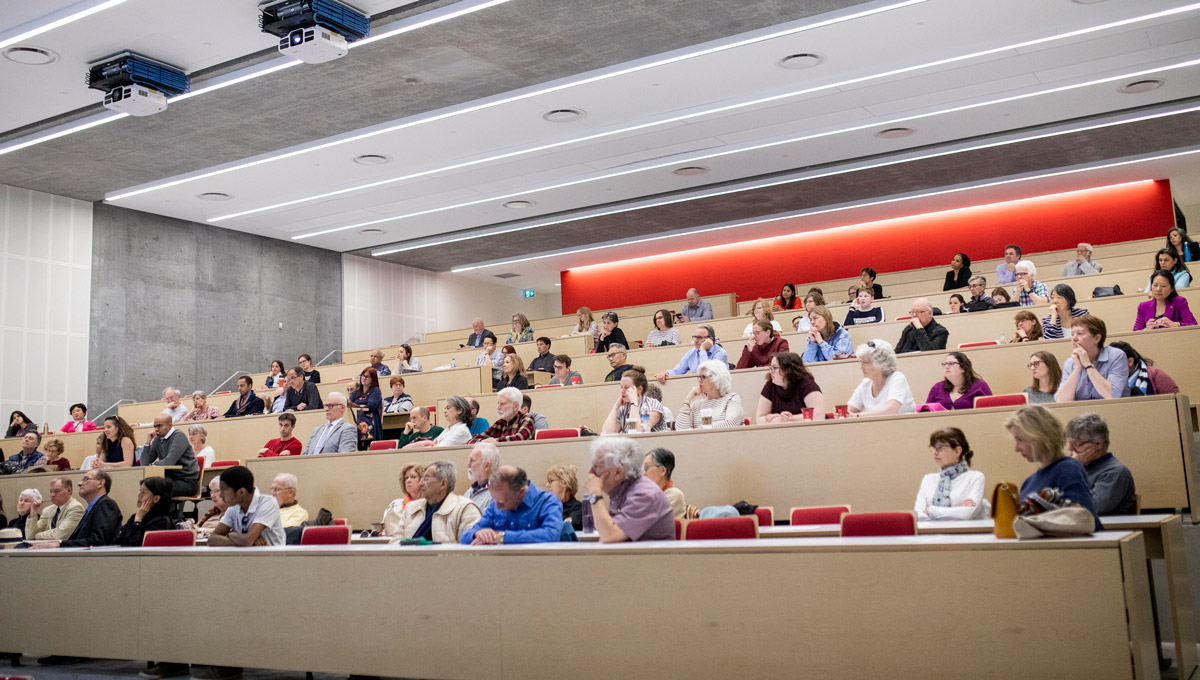 The audience in a large theatre in the Health Sciences Building listens to President Bacon.