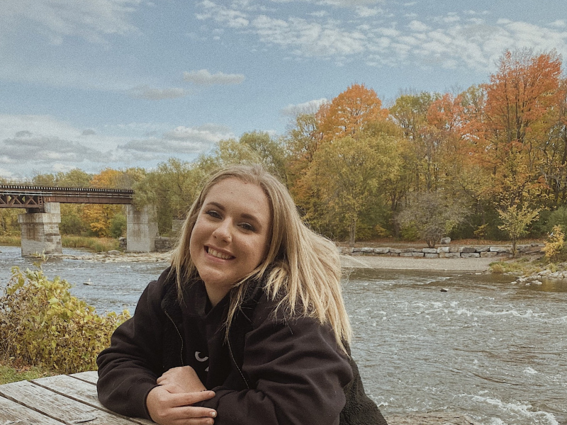 A young woman smiles for the camera while sitting by a riverbank
