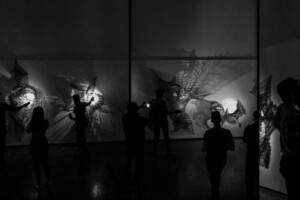 Guests shine light through sculptures from the Diluvio exhibition in a dark room.