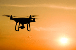 A drone flies in the sky in front of a setting sun.