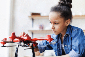 A girl sits at a table and holds a drone.