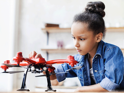 A girl sits at a table and holds a drone.