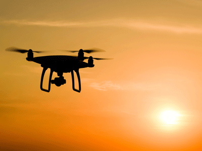 A drone flies in the sky in front of a setting sun.