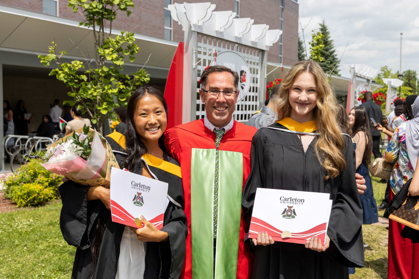 A professor and two students take a photo outside following a convocation ceremony.