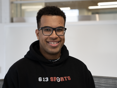 A young man wearing glasses and a black hoodie smiles for the camera.