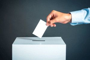 A person's hand is shown depositing a ballot into an election ballot box.