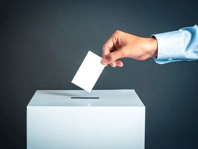 A person's hand is shown depositing a ballot into an election ballot box.