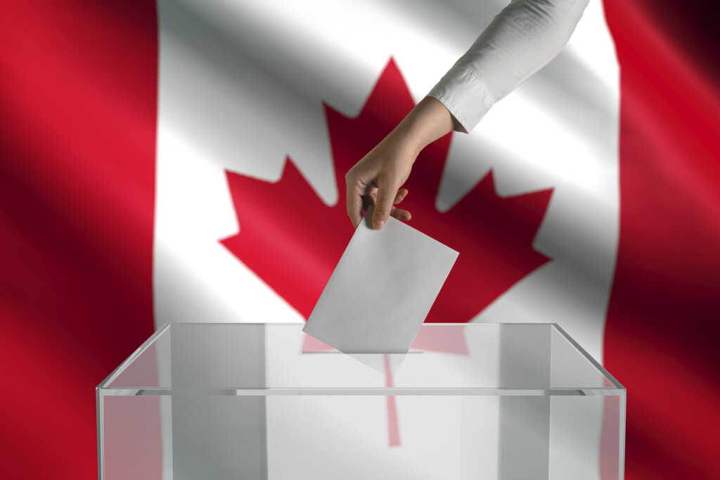 A hand places a voting card into a box over a backdrop of a Canadian flag.