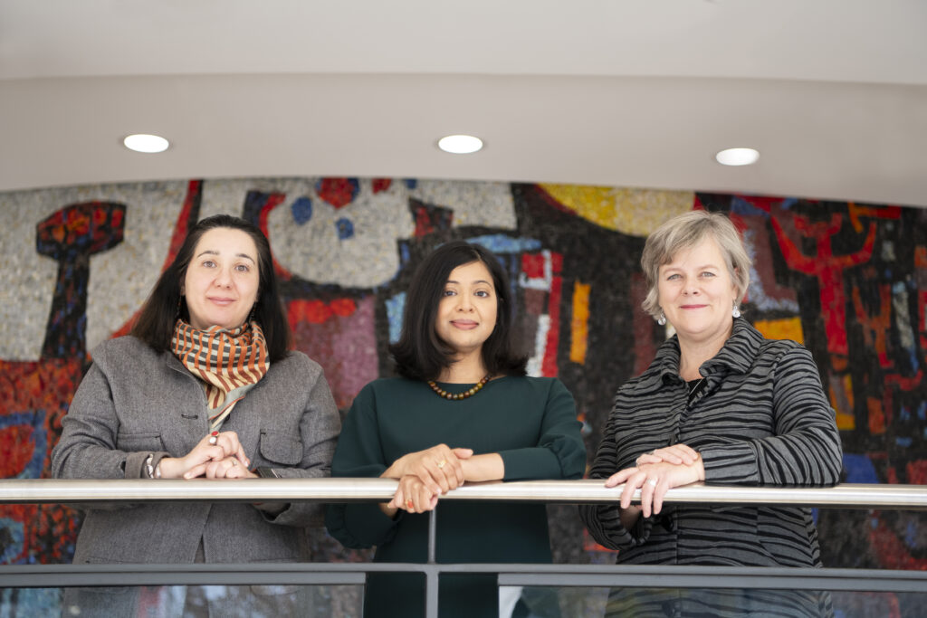 Three women pose for a photo together while leaning on a railing.