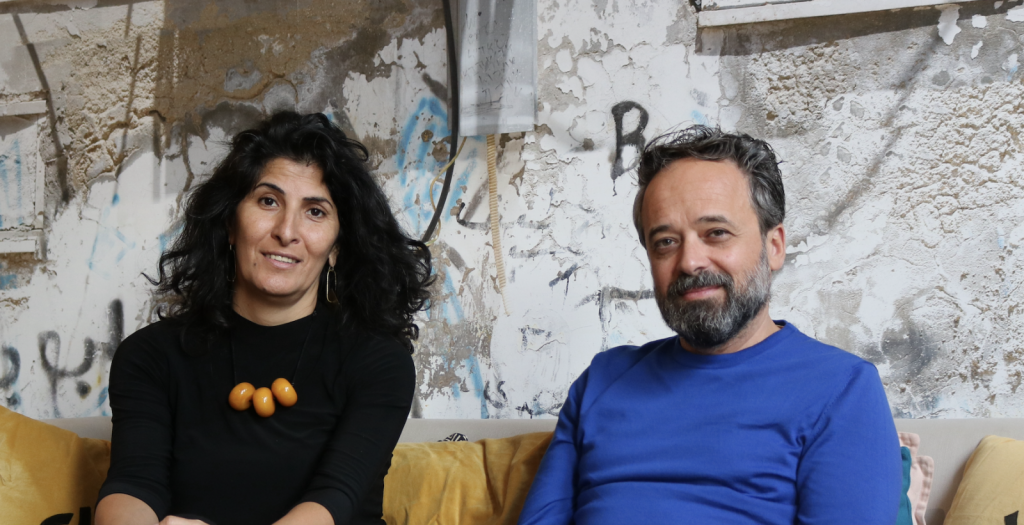A man and a woman sit on a couch and smile for the camera.