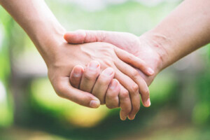 Two people hold hands in front of a grassy background.