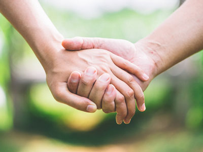 Two people hold hands in front of a grassy background.