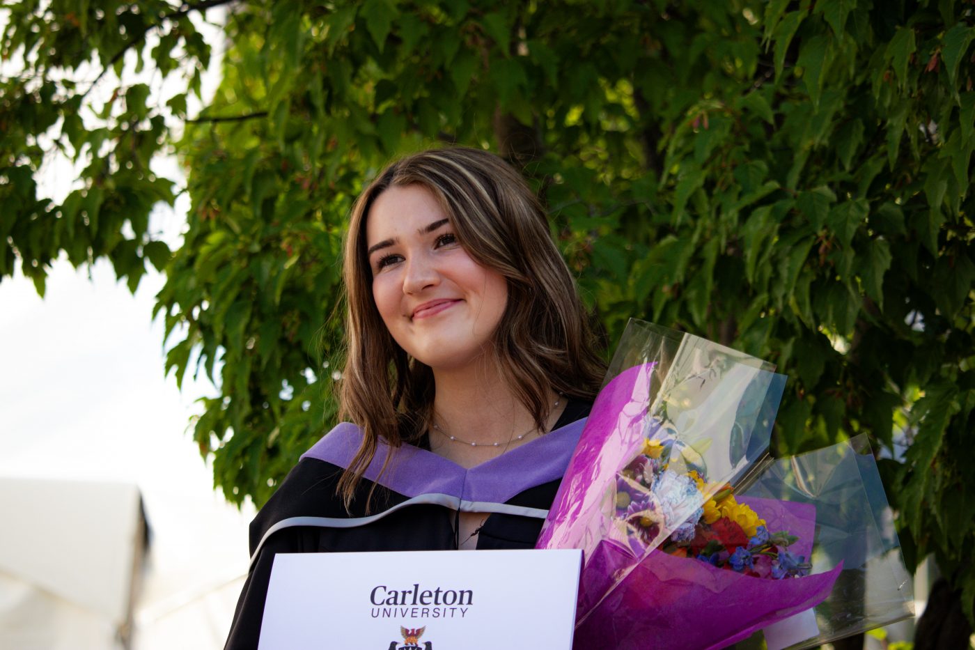 A graduating student poses with her degree and bouquet outside the Athletics Building.