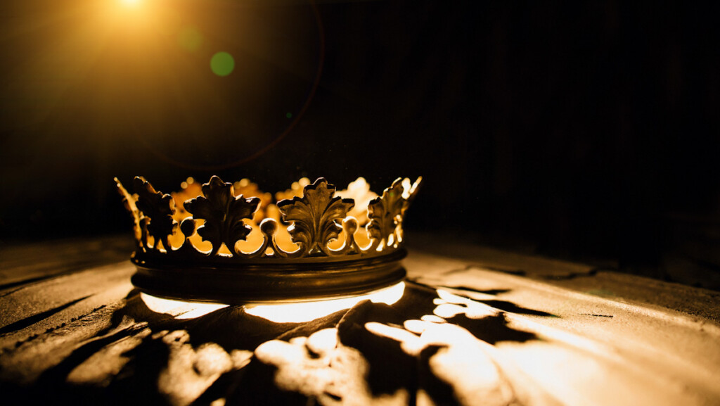 An image of a crown. Light streaming behind golden metal crown casting a shadow.