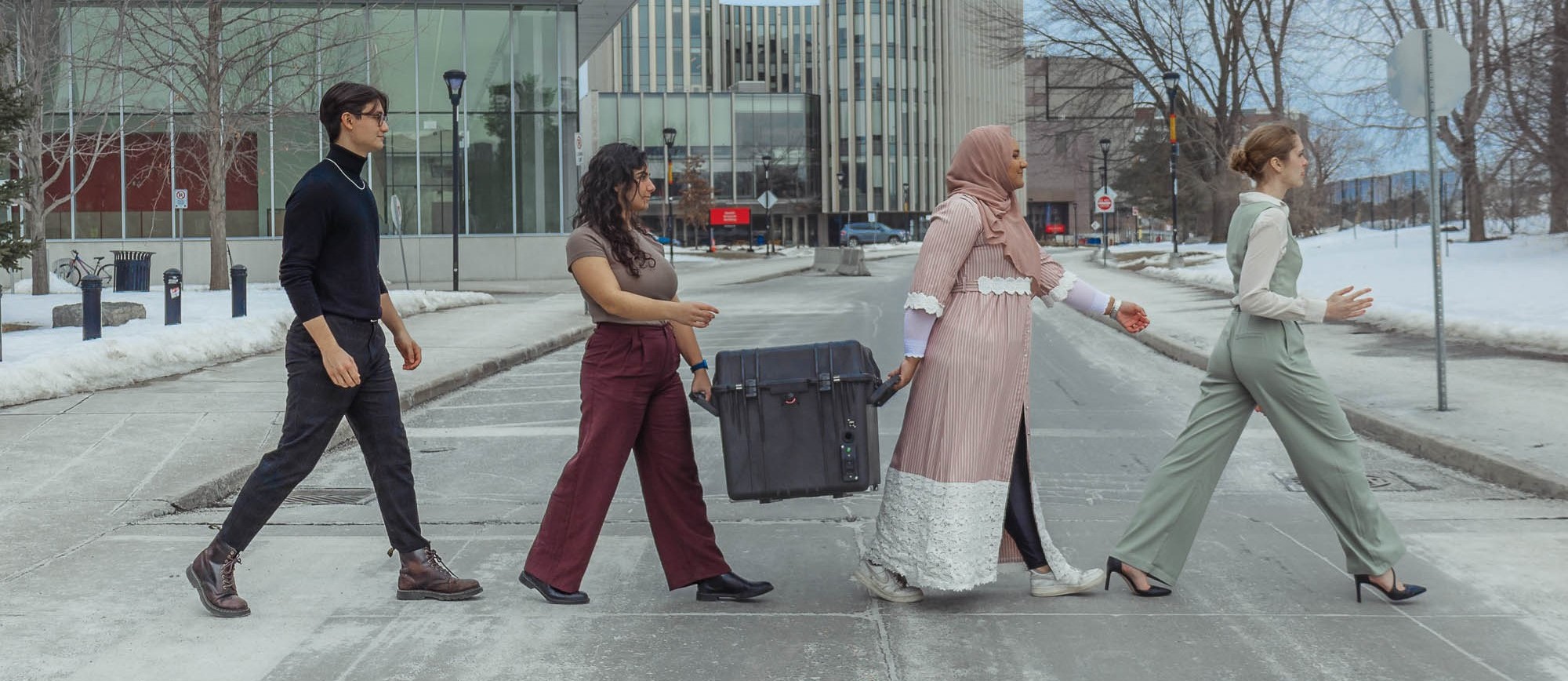 Four students walk across a crosswalk holding a black case