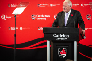Premier Doug Ford standing at a podium in front of a red backdrop