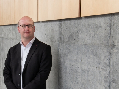 Martin Geiger poses against a cement and wood wall in the Health Sciecnes Building.