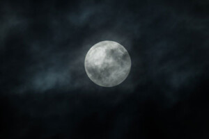 The moon shines in the night sky surrounded by clouds.