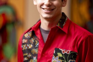 A man in a red shirt with black hair smiles at the camera
