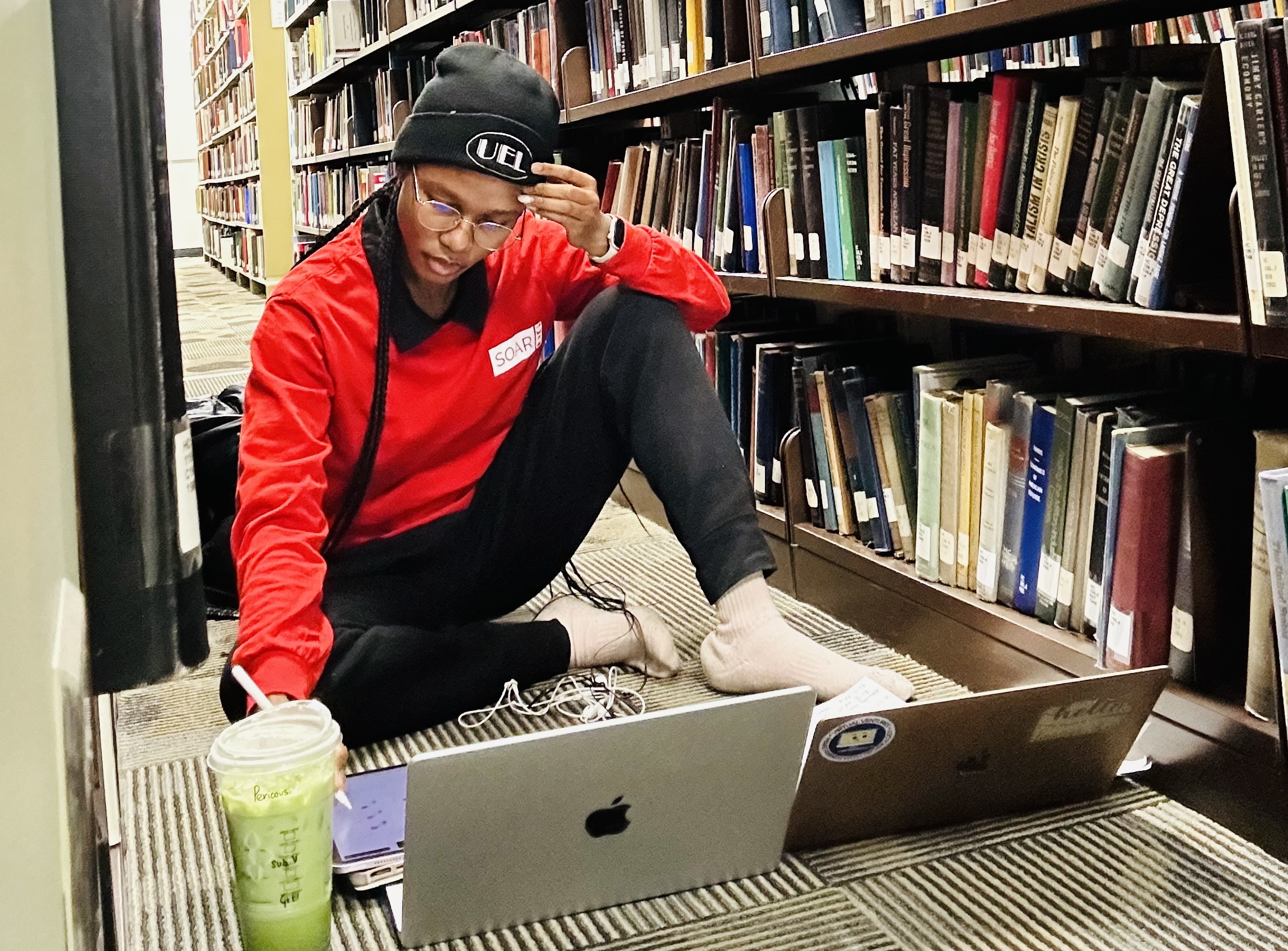 Precious Kolawole studying AI and health on the lirbrary floor with multiple laptops